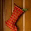 Gingham stocking in red/terracotta with greenery on wood panel background.