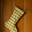 Gingham stocking in olive/sage with greenery on wood panel background.