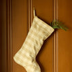 Gingham stocking in ivory/flax with greenery on wood panel background.