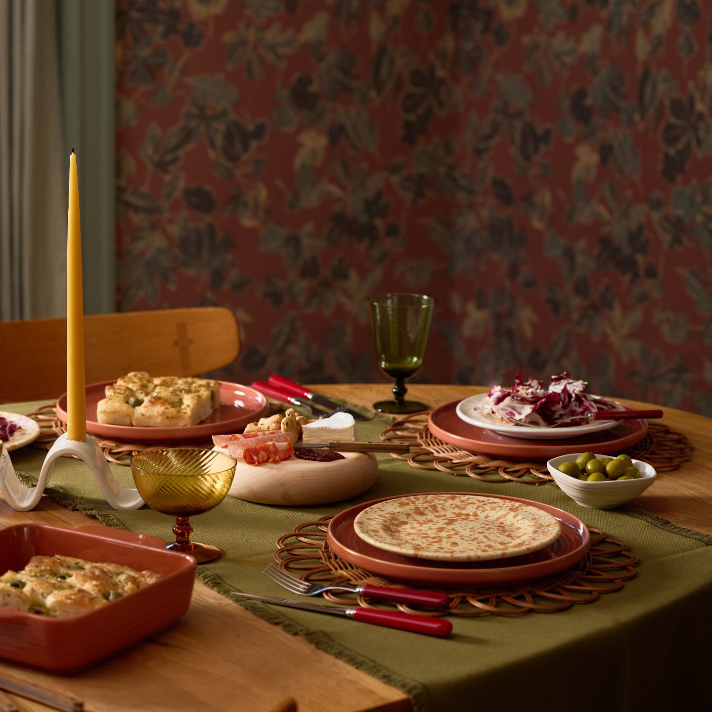 Tablescape with olive runner, place settings, taper candle, glassware, taper candle.