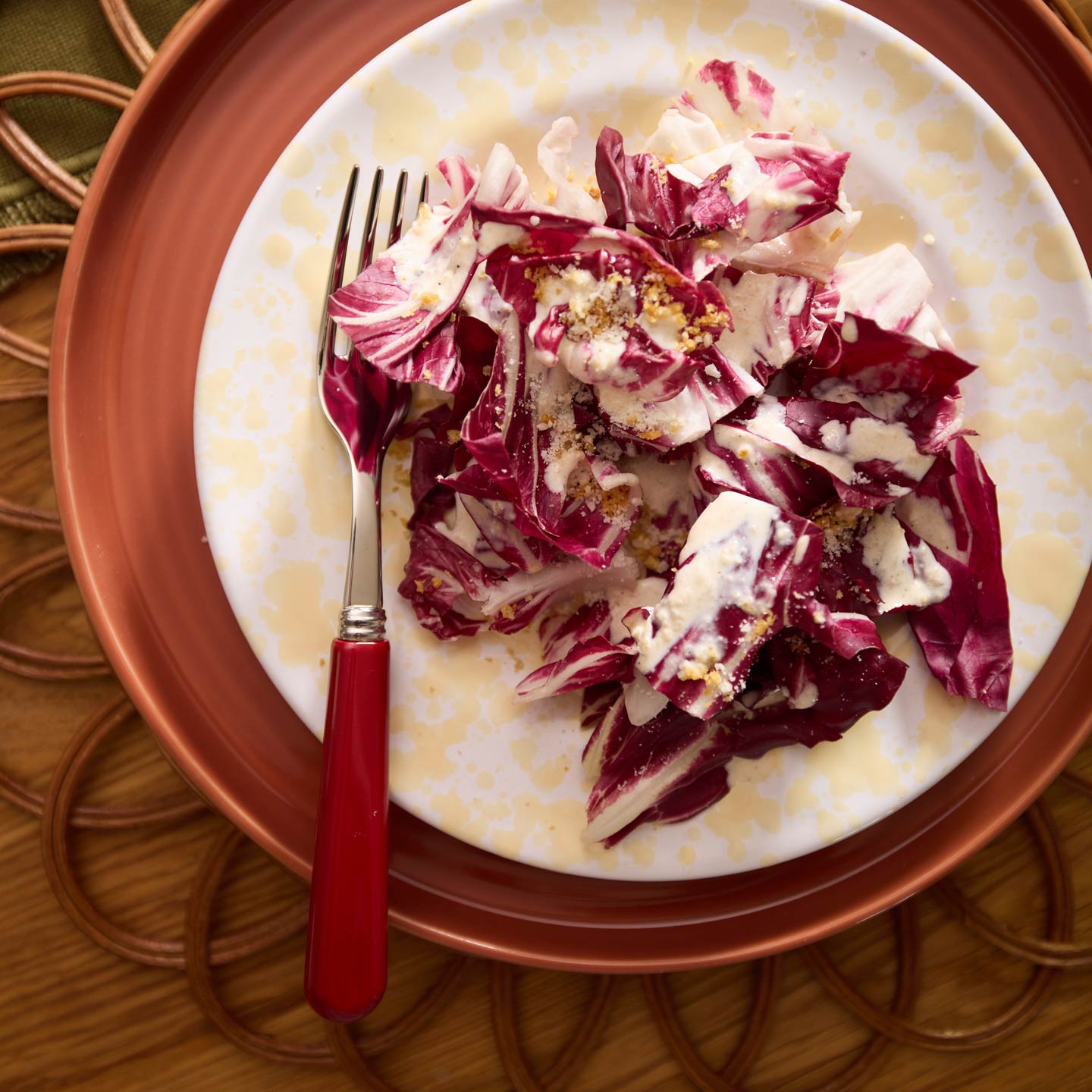 Salad on splatter plate with sabre red fork and rattan placemat.
