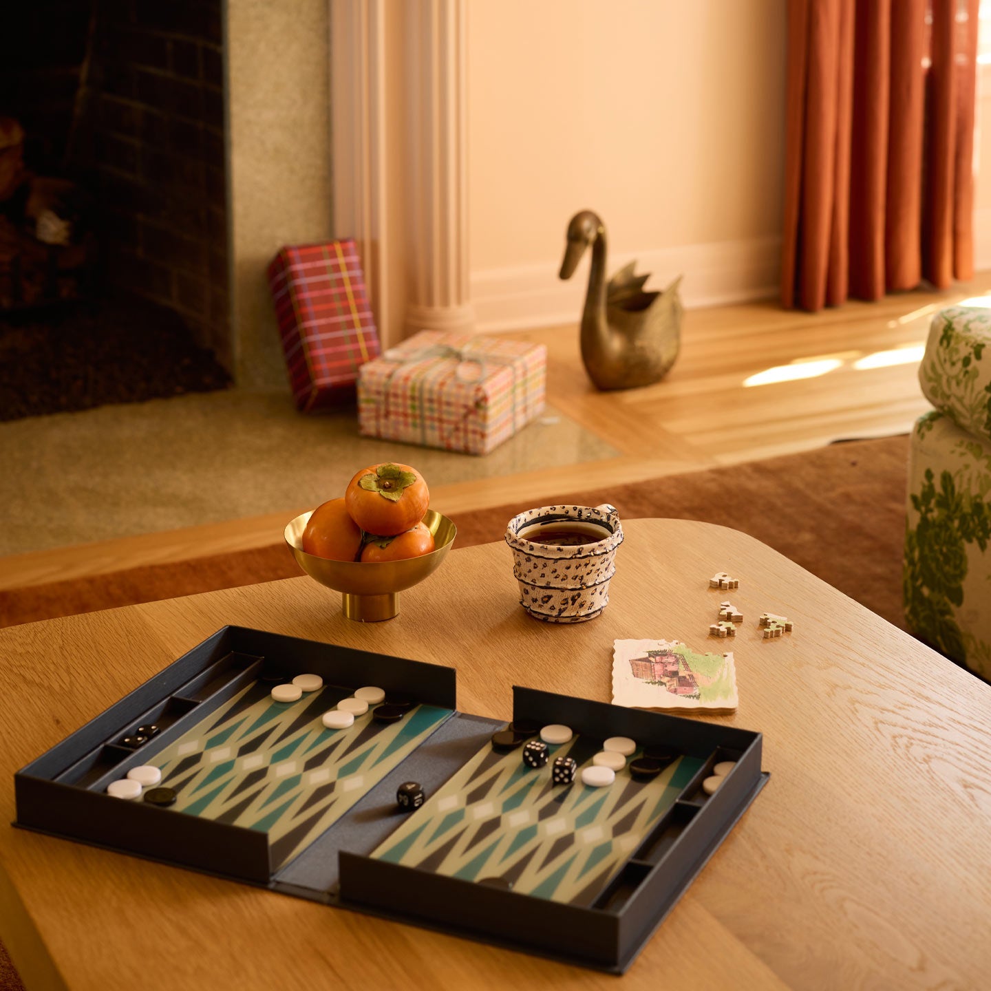 Coffee table in living room with open backgammon game, puzzle, mug, and footed bowl with fruit.