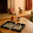 Coffee table in living room with open backgammon game, puzzle, mug, and footed bowl with fruit.