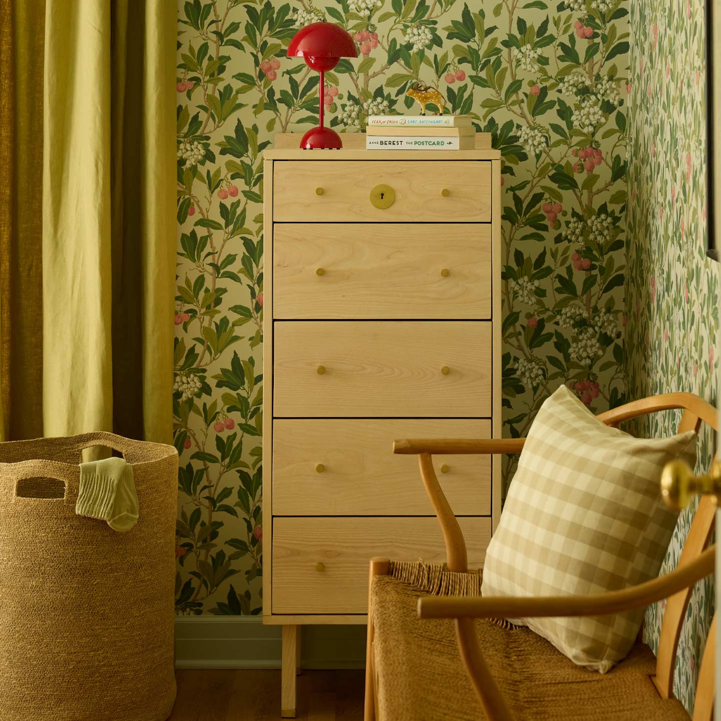 Bedroom with wood dresser and red lamp, chair with gingham pillow, and laundry basket