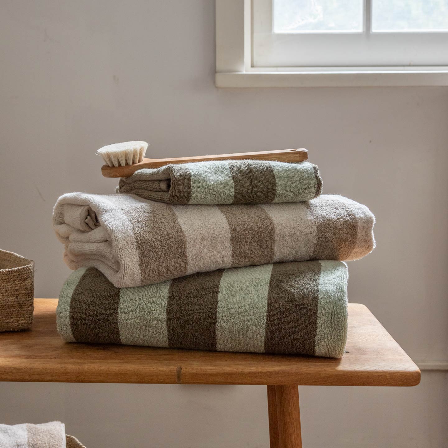 Stack of striped towels on a wooden table with a brush