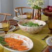 Table with mustard table runner, place settings, salad bowl, platter with carrots, and pitcher with flowers.