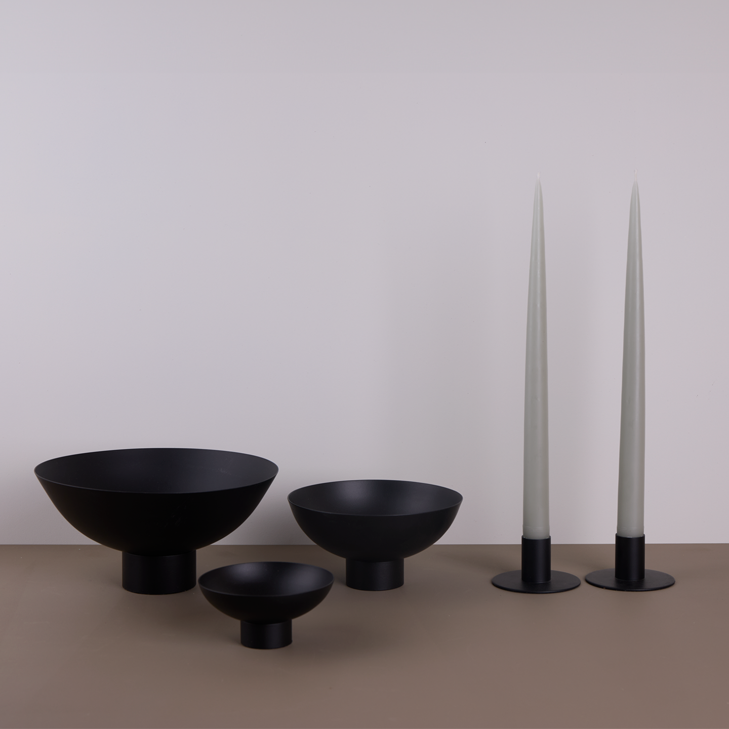 A trio of footed bowls and pair of candle holders, all in Black, with grey taper candles.