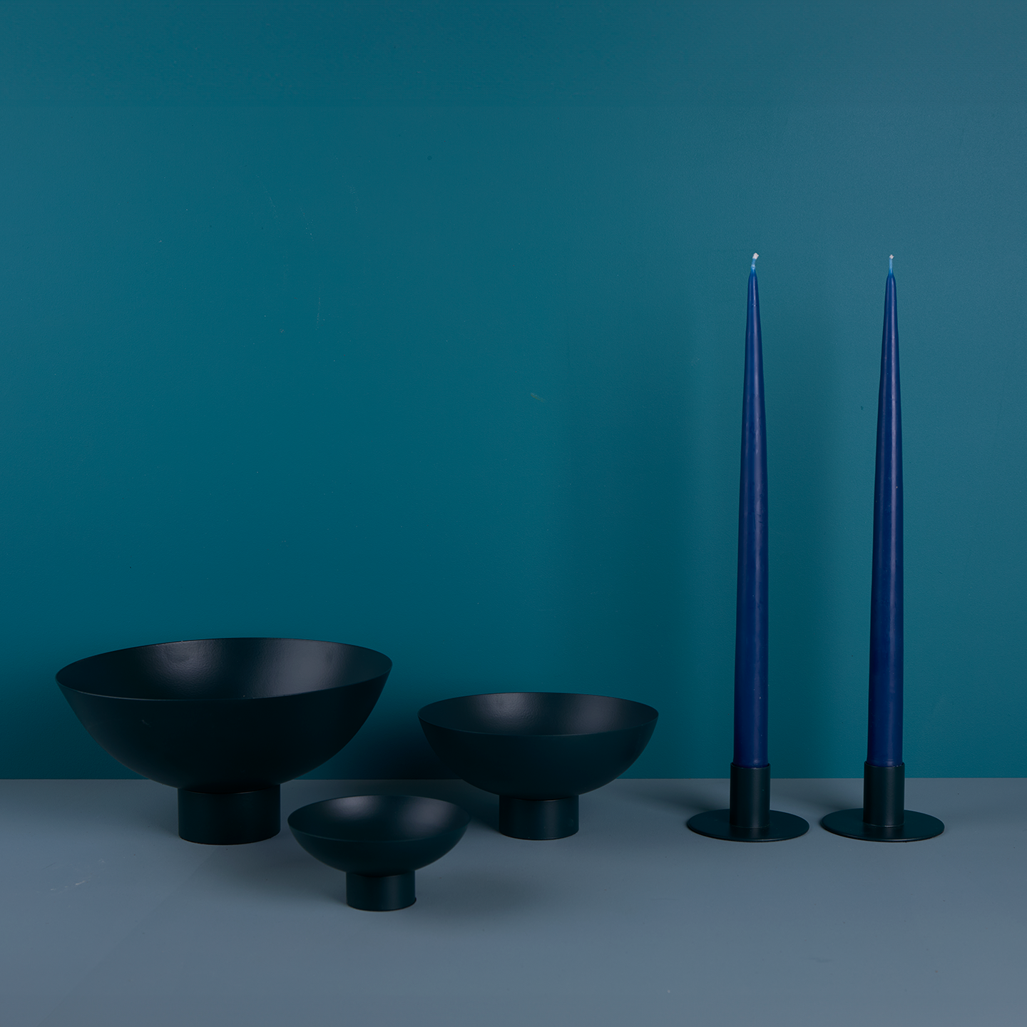 A trio of footed bowls and pair of candle holders, all in Peacock, with blue taper candles.