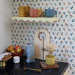 Coffee setup in kitchen with mugs, shelf, coffee, bowl of apples and floral background.