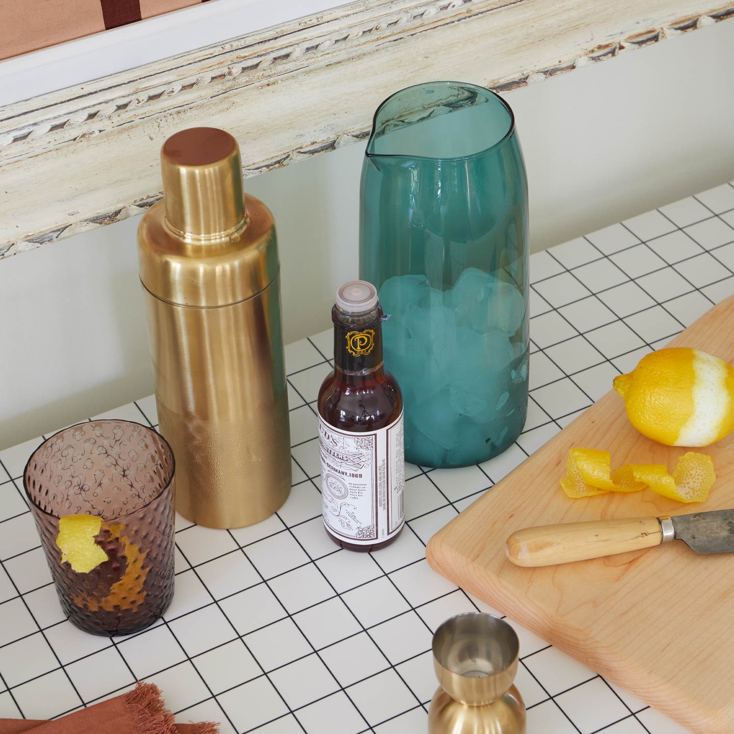 Bartending setup with gold shaker, blue glass, and lemon on a tiled bar counter.