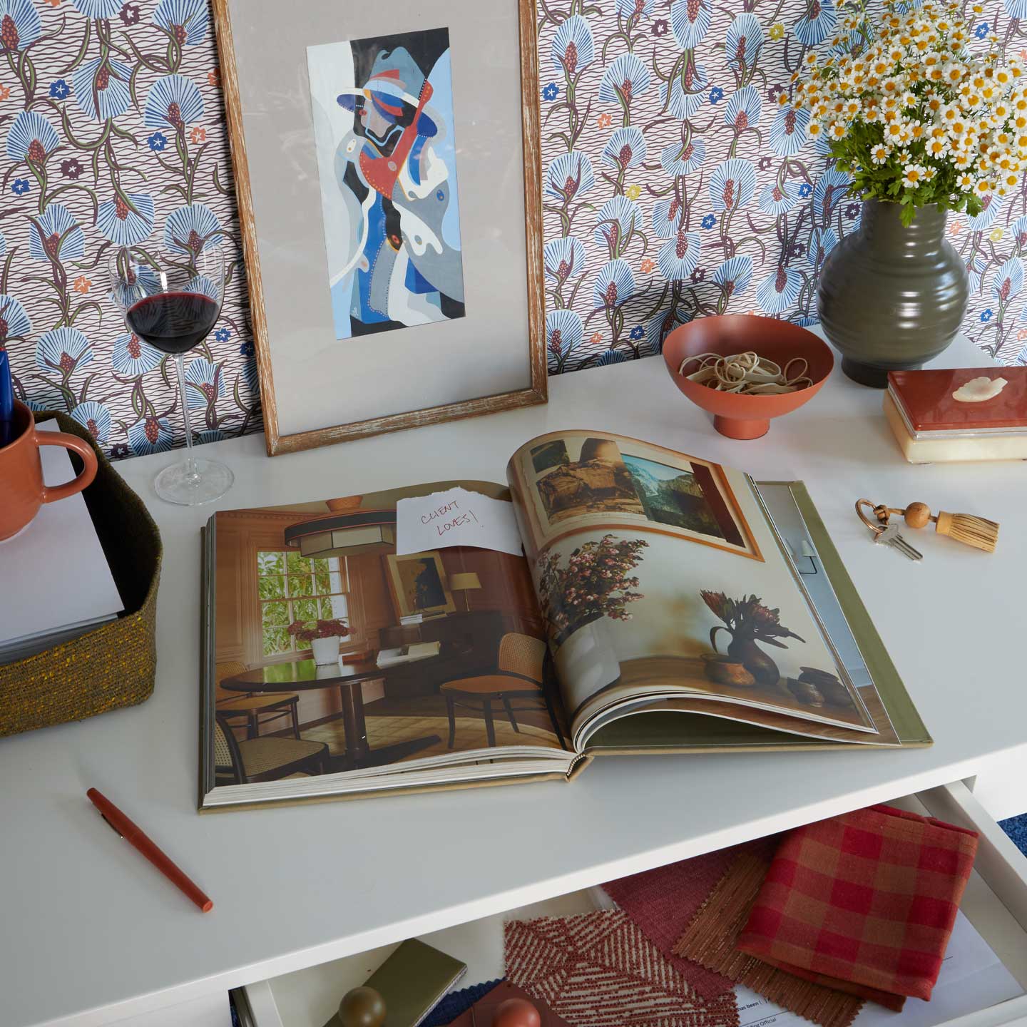 Open book on a table with decorative items including a vase, glass, and framed art.