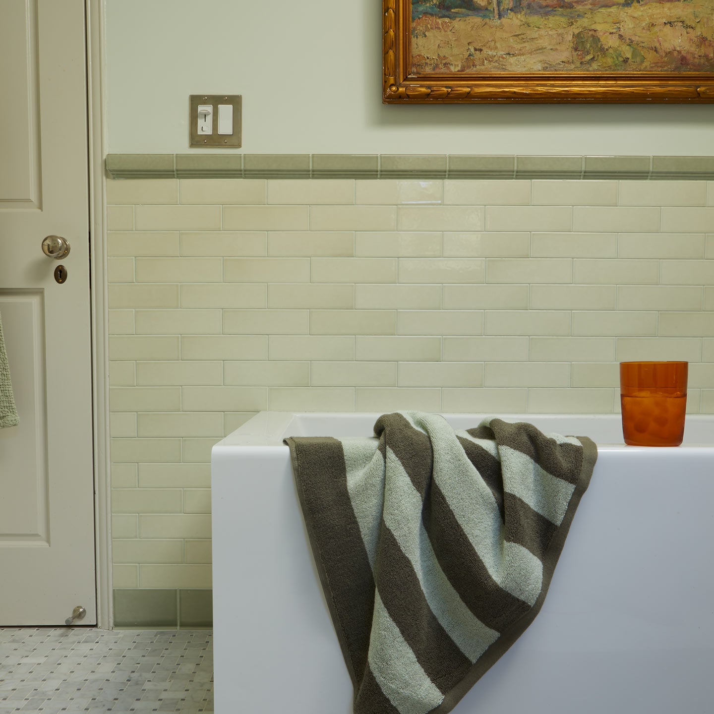 Bath scene with Olive Striped Towel on bathtub and Essential Glass in Terracotta.