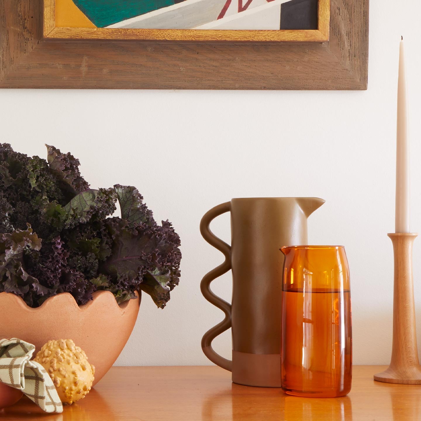 Essential Glass Pitcher in Terracotta with stoneware pitcher and bowl with greens and candle holder on wood surface.