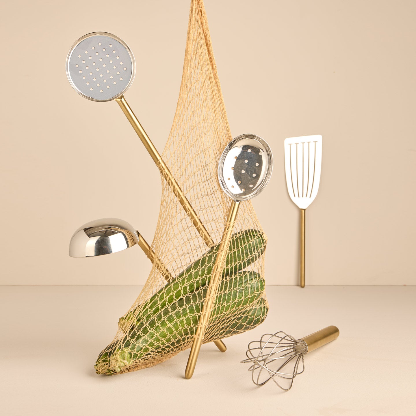 Simple metal kitchen tools in brass with net and squash on warm background.