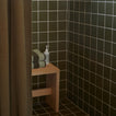 Tiled shower with olive shower curtain and wooden bench with towels and soap.