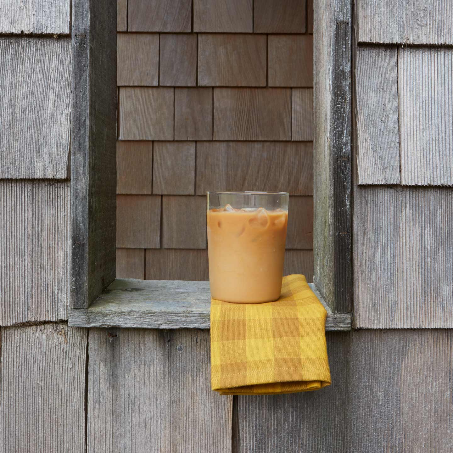 Glass of iced coffee on ledge on Essential Gingham Napkin in Mustard.