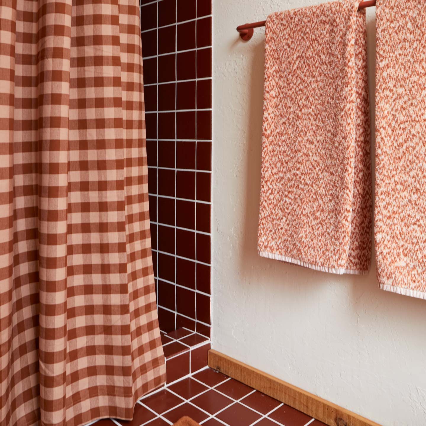 Essential Gingham Shower Curtain in Terracotta with terracotta tiled shower and Space Dye Bath Towels hanging on a towel bar.