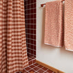 Essential Gingham Shower Curtain in Terracotta with terracotta tiled shower and Space Dye Bath Towels hanging on a towel bar.
