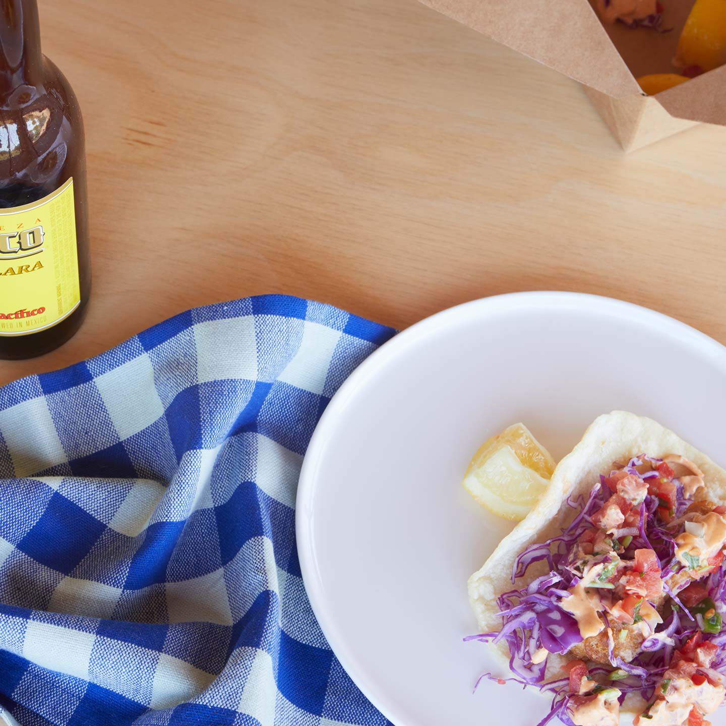 Tabletop close up with Simple Porcelain Plate with taco and Essential Gingham Napkin in Blue.