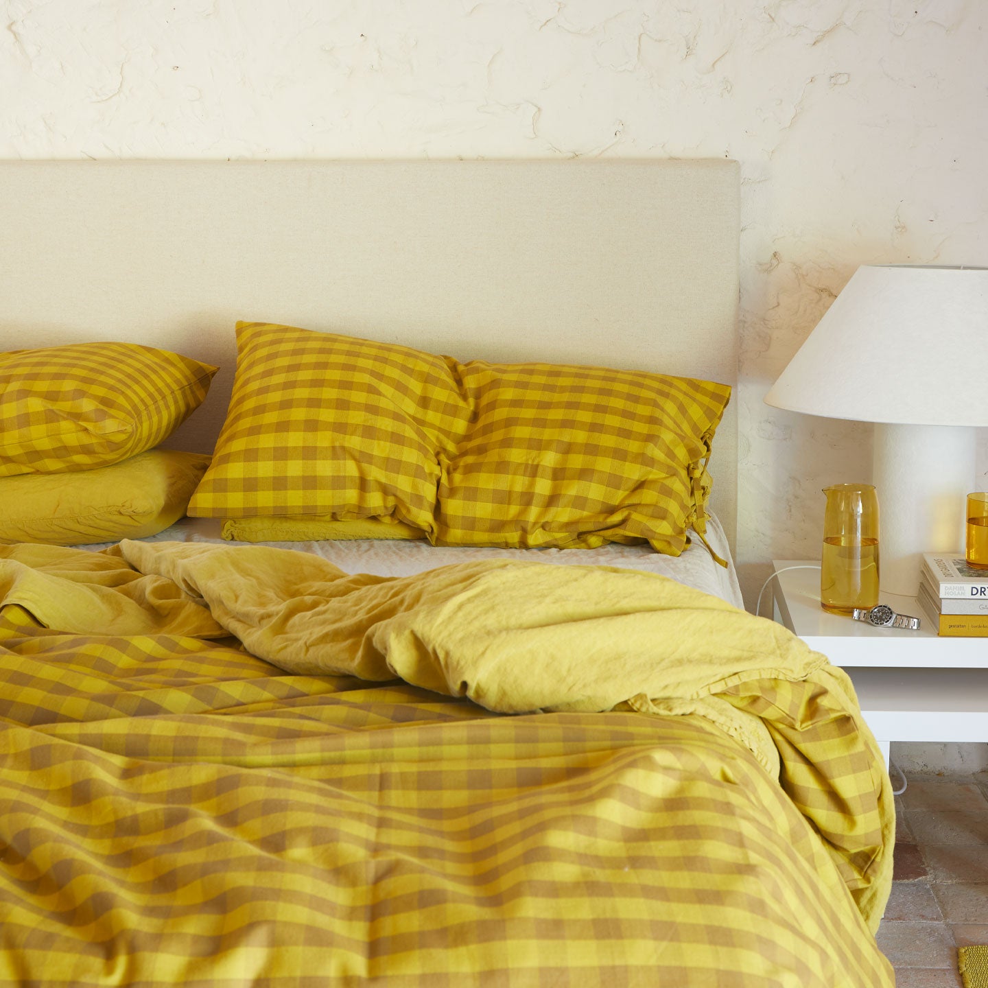 Bed with mustard bedding in solid and gingham with nightstand.