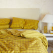Bed with mustard bedding in solid and gingham with nighstand.