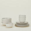 A neatly stacked set of white dinnerware includes plates, bowls, and small bowls against a plain background.