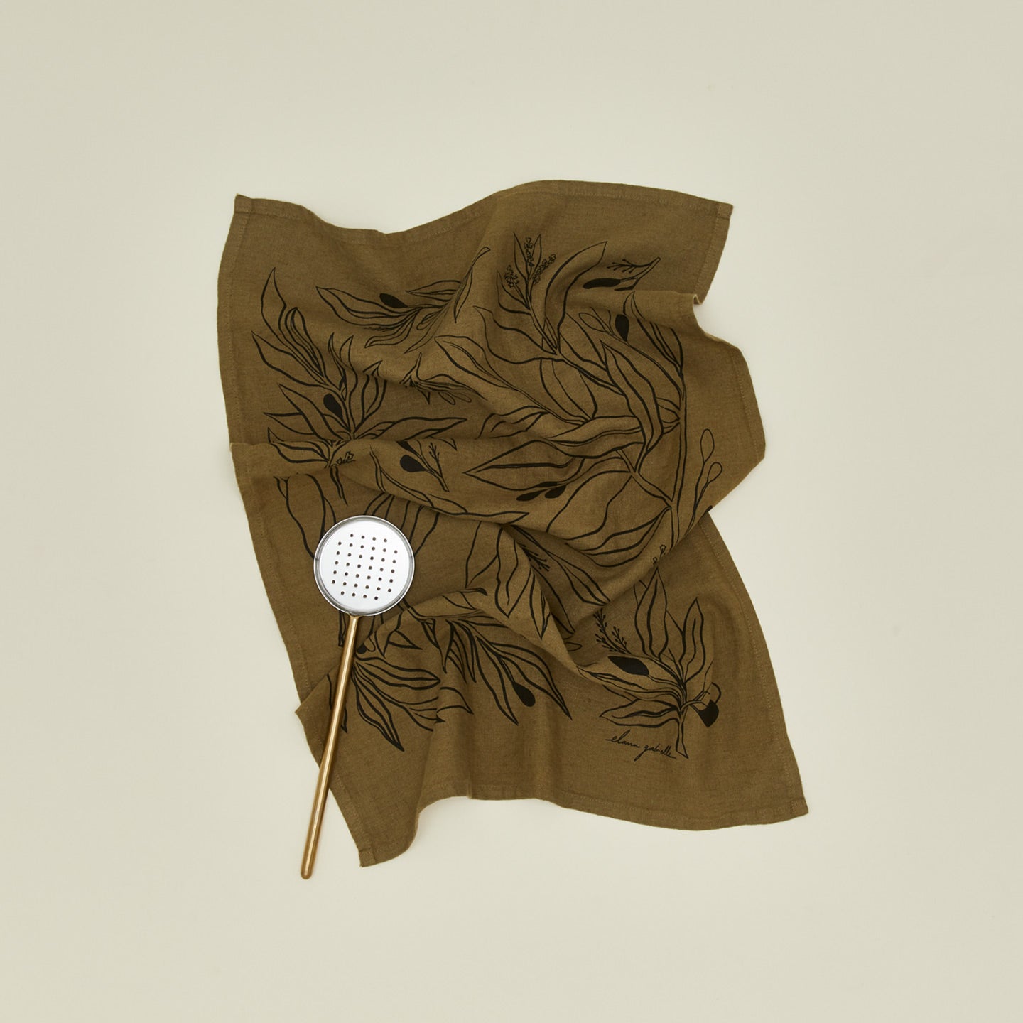 Linen tea towel with olives with slotted flat spoon.