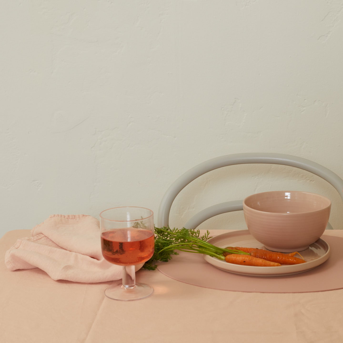 Glass of pink drink with carrots and a bowl on a pink surface