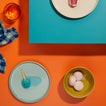Colorful table setting with plates, bowls, and a glass on a multicolored background