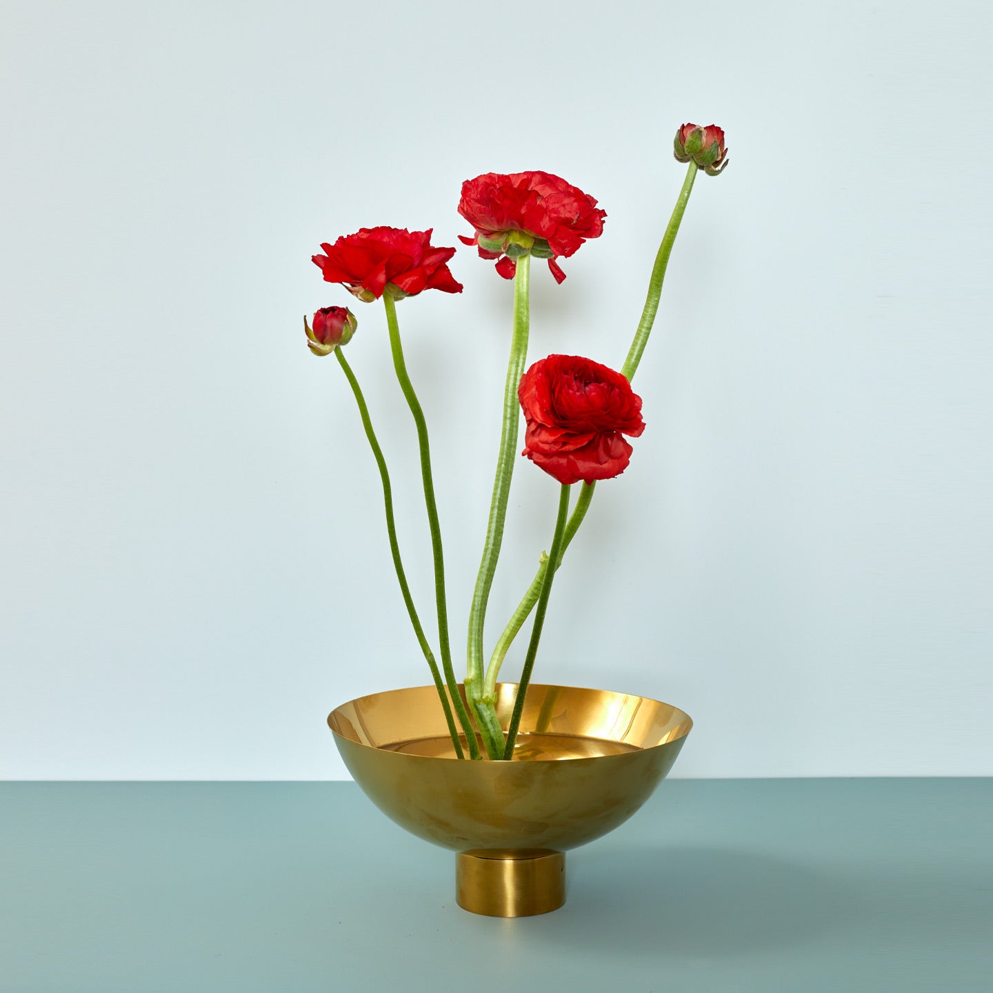 Brass footed bowl with red flowers on blue background.