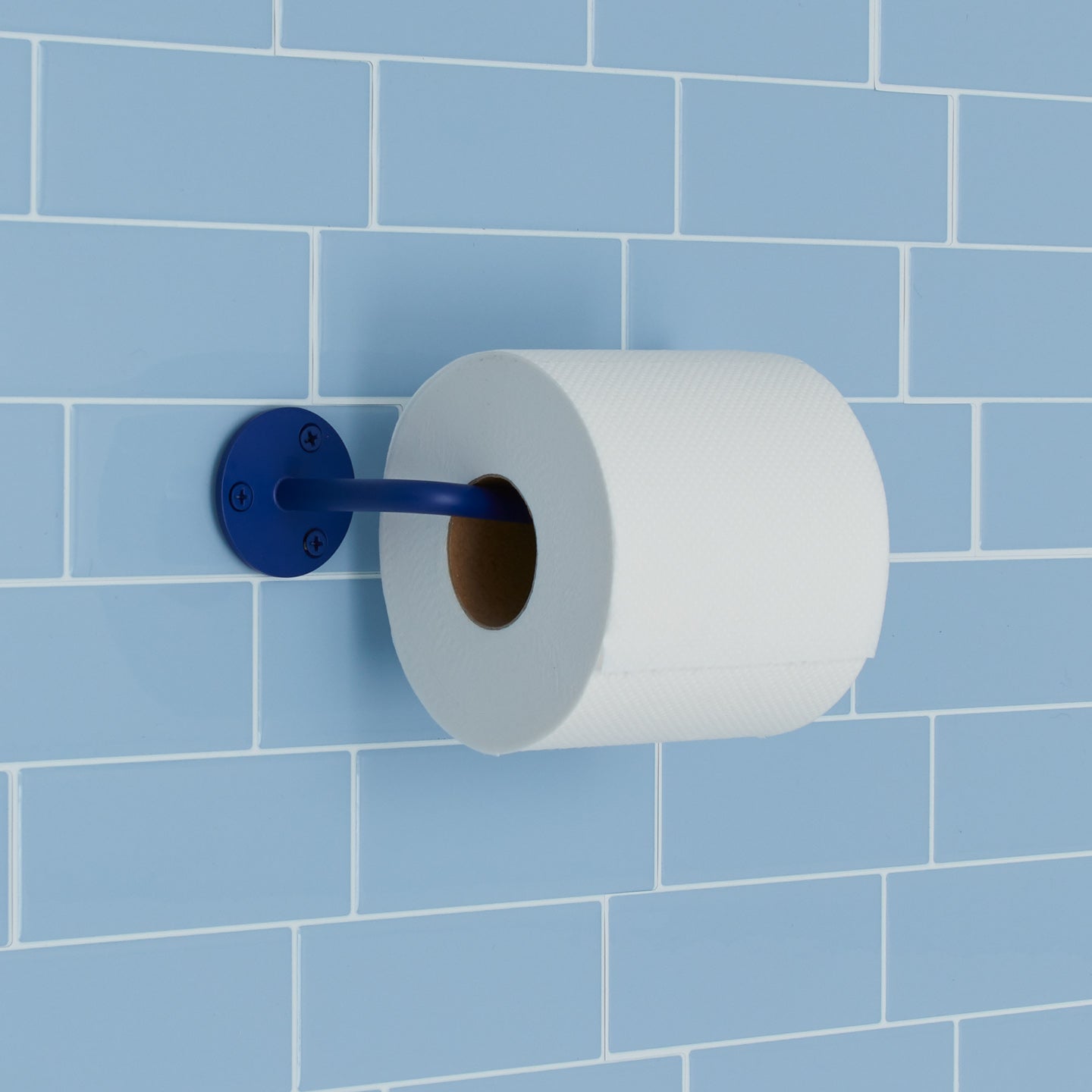 Essential toilet paper holder in klein blue on light blue tile background.