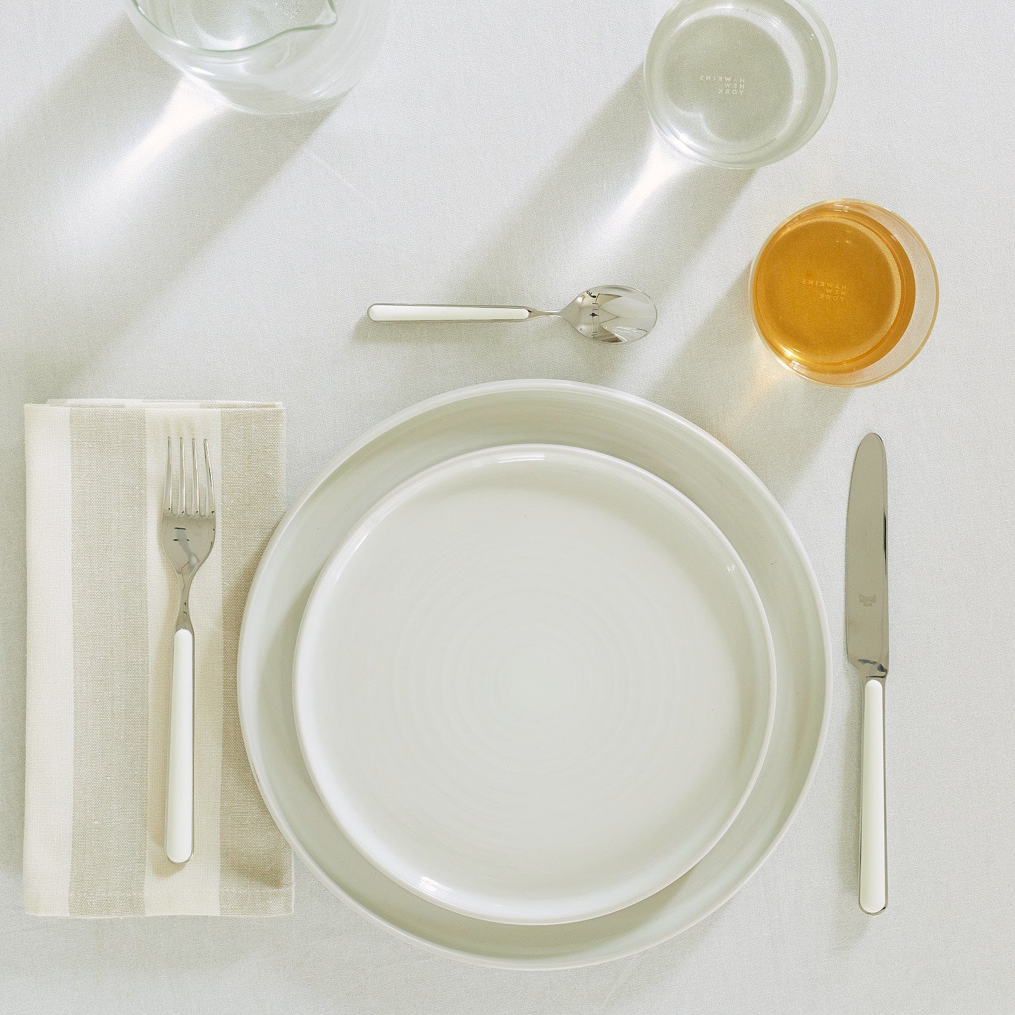 Placesetting with Essential Striped Dinner Napkin in Ivory and Flax on ivory tablecloth.