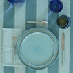 Placesetting with Essential Dinner Napkin in Sky on blue striped tablecloth.
