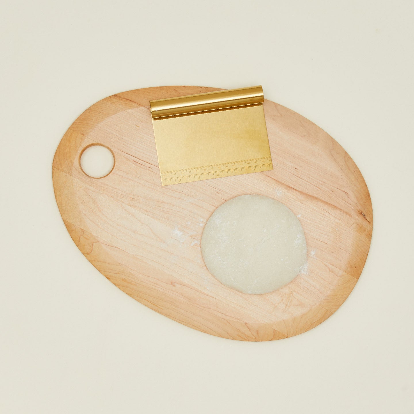 Brass dough scraper on a wood cutting board with dough.