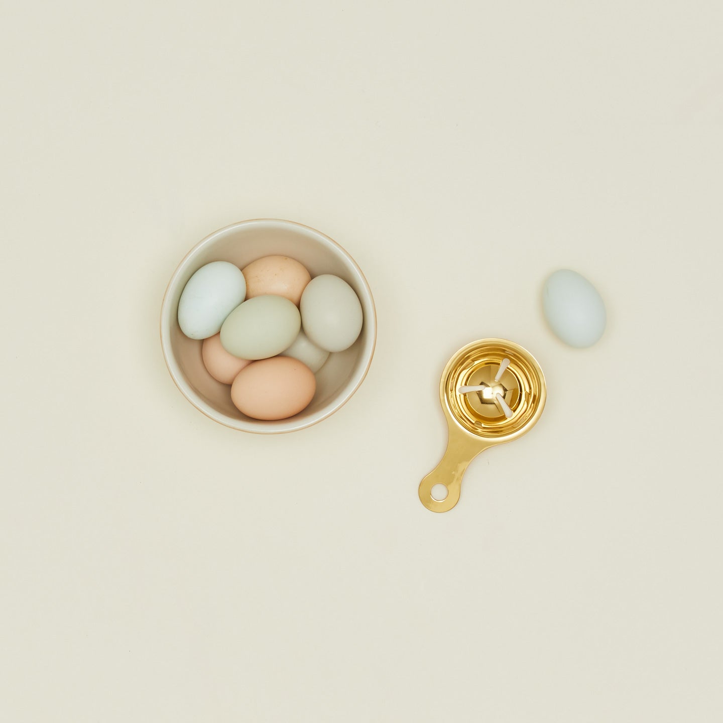 Brass egg separator on a beige background with a bowl of colorful eggs.