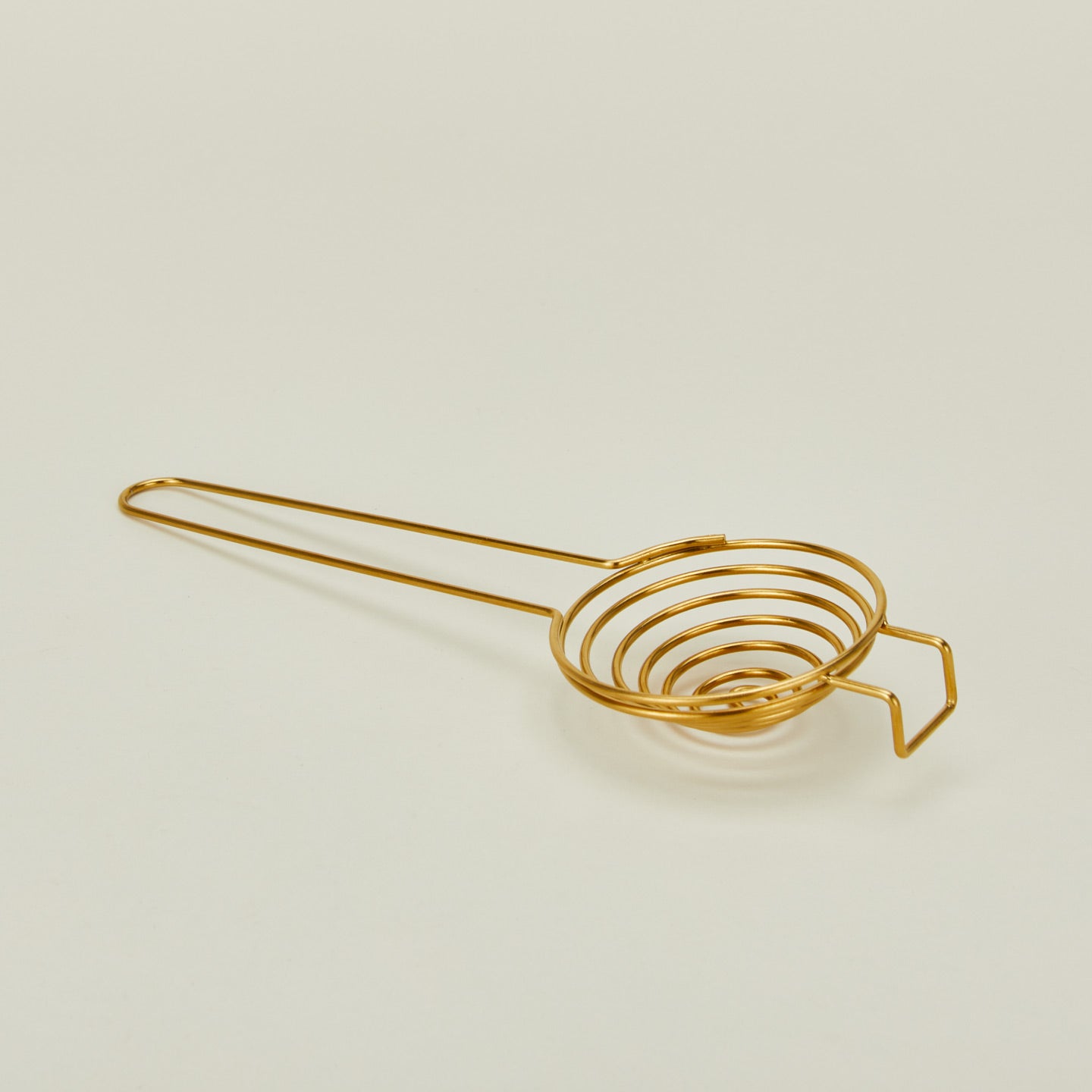 Brass swirl egg separator close up on ivory background.