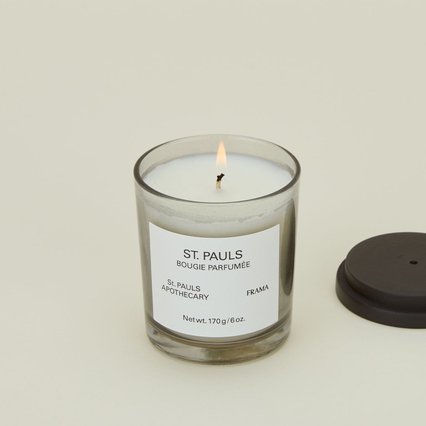 A close up of a lit wax candle with the scent St. Pauls.