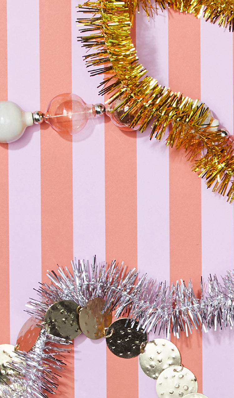 Tinsel garlands and bead strings lie on a pink and white striped background.