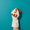 Hand wearing rubber glove squeezing soapy red sponge on blue background.
