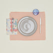 A table setting with grey plates, a blue glass, a blush placemat, and a rose patterned napkin.