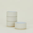 Four beige ceramic bowls are stacked vertically on the left, with a single bowl placed to the right on a light cream background.
