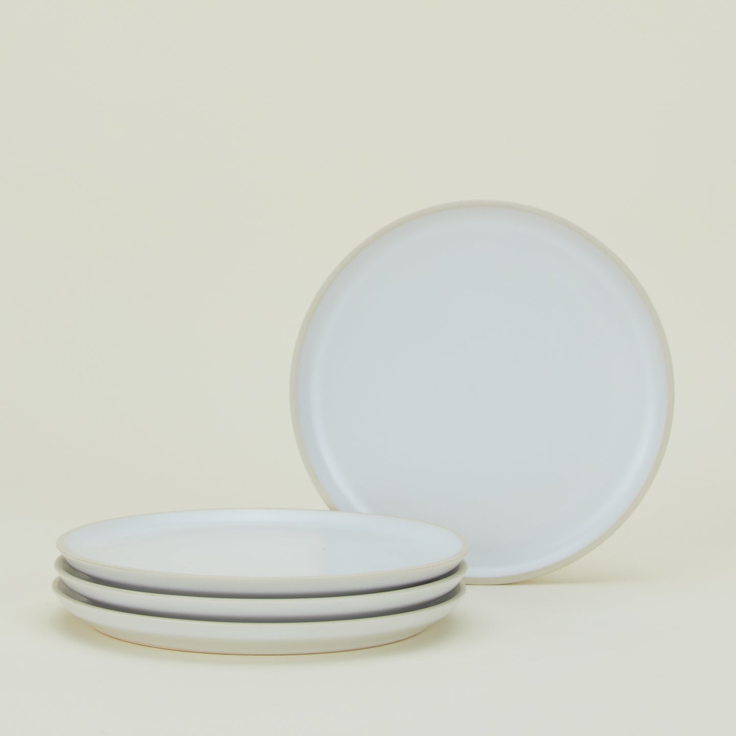 Four white ceramic plates, with three stacked and one upright behind them, against a light background.