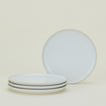 Four white ceramic plates, with three stacked and one upright behind them, against a light background.