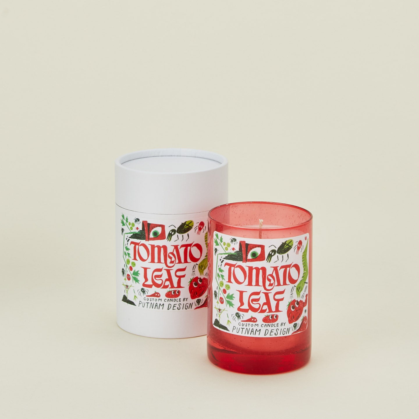 Candle with 'Tomato Leaf' design and white cylindrical container on a beige background