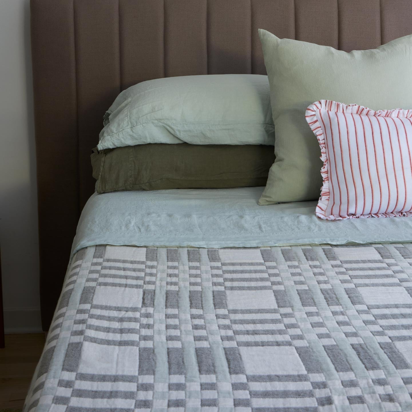 Bed with green bedding and red striped pillow.