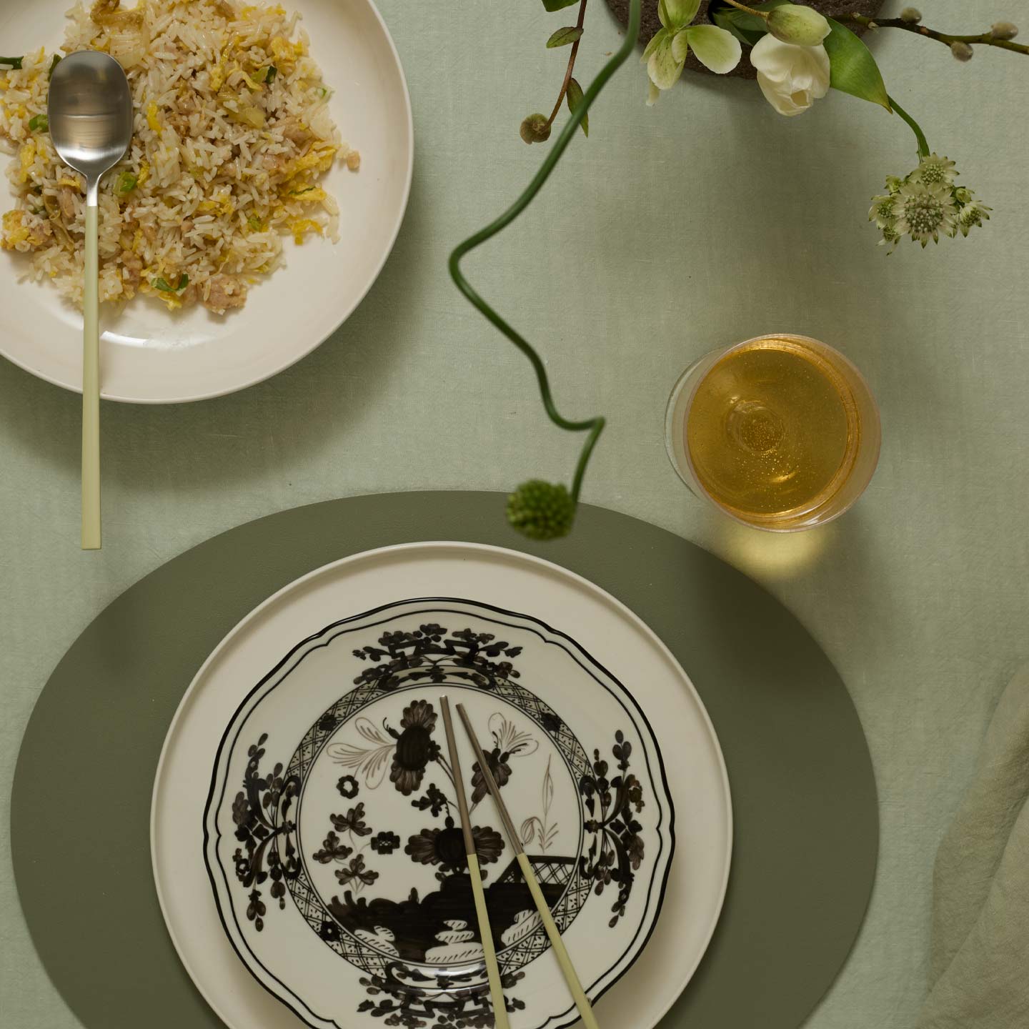 Table setting with a plate of food, a glass of wine, and a vase of flowers on a green tablecloth.
