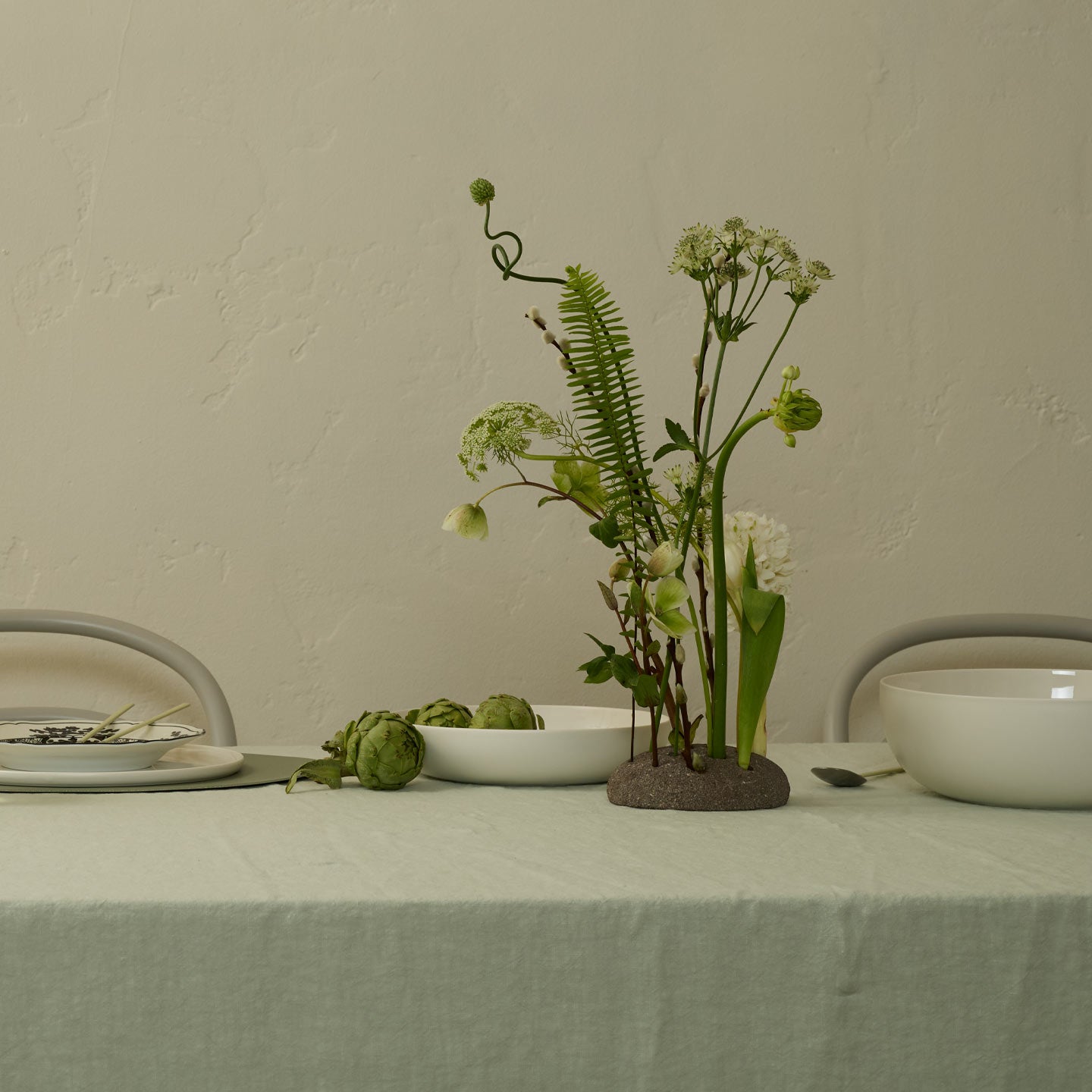 Table setting with a vase of greenery and white flowers on a light green tablecloth.