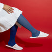 Person wearing blue knee-high socks and white bath slippers and bathrobe on a red background